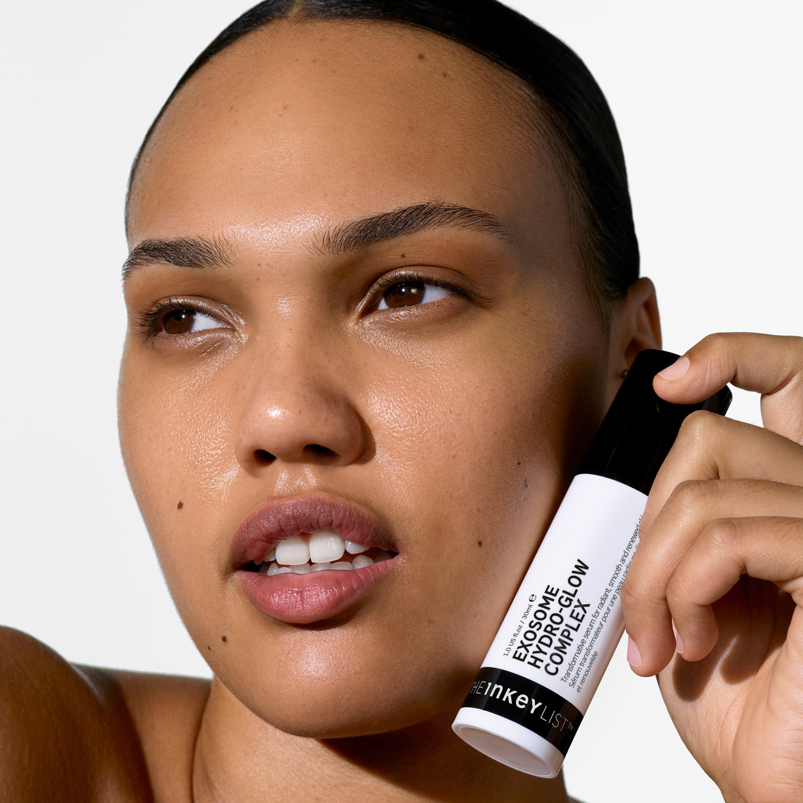 Woman holding Exosome Hydro-Glow Complex close to her face against a white background