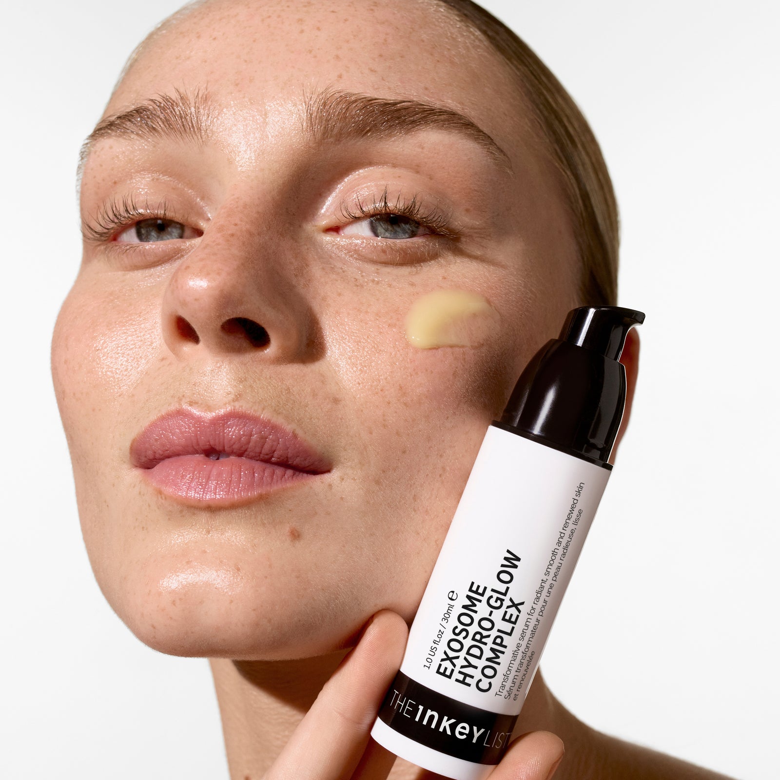 Woman applying Exosome Hydro-Glow Complex product to her face with a white background