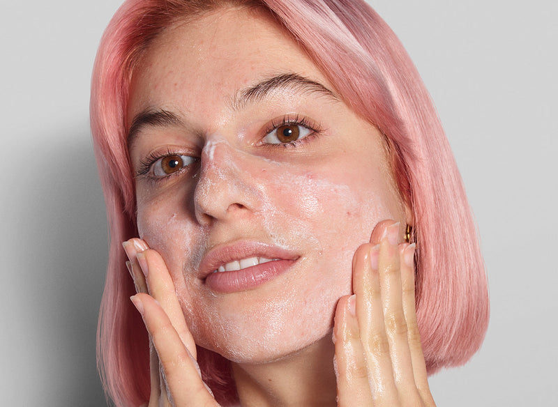 Model with pink hair applying skincare 