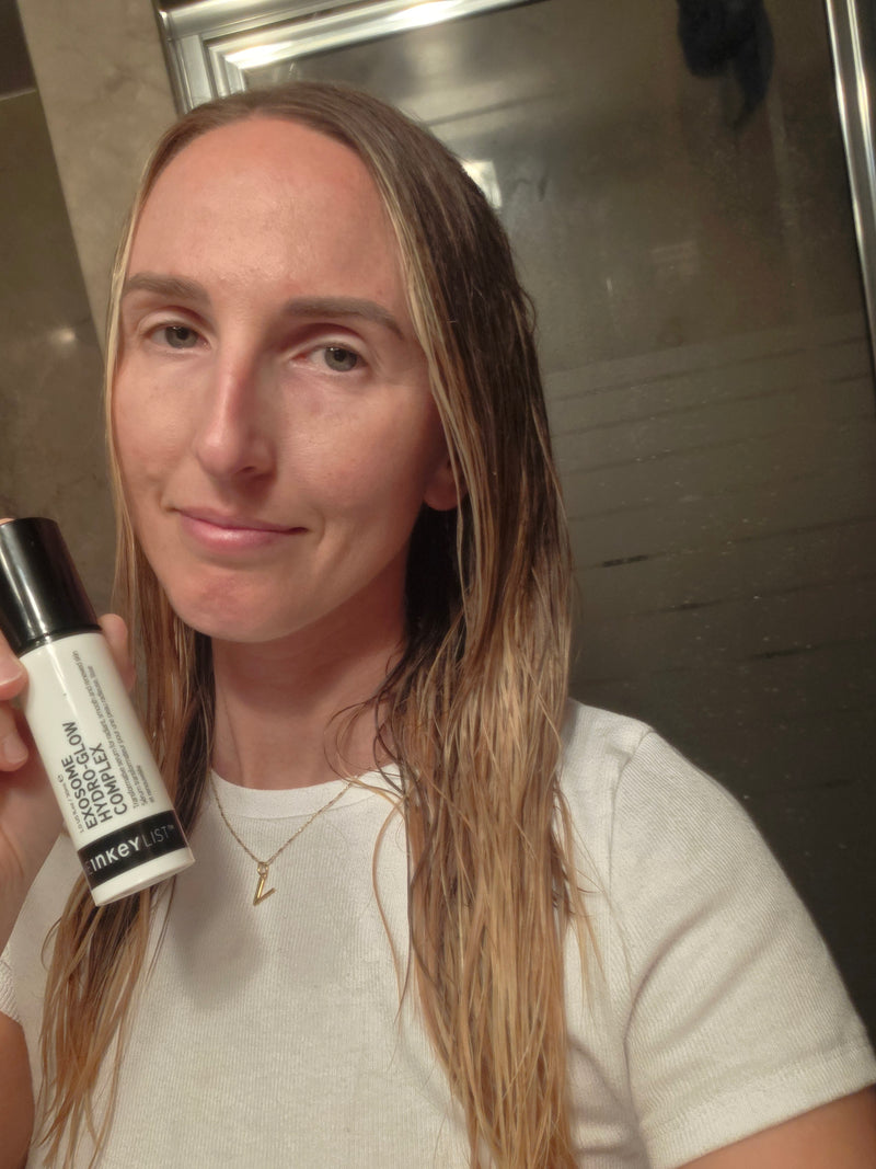A woman holding a bottle of Exosome Serum to her face in a bathroom background