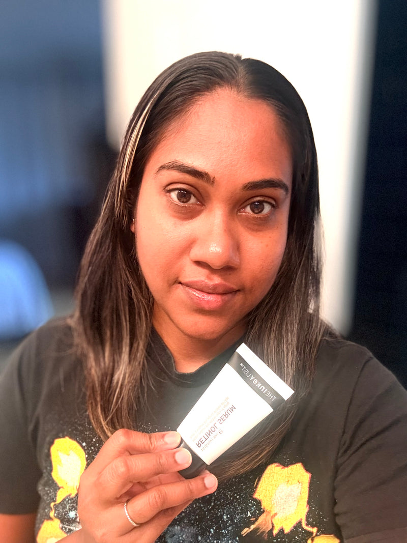 A woman holding a small white and black retinol serum in front of her face.