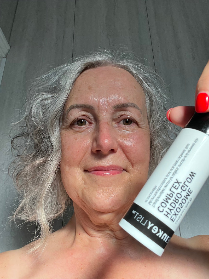 A woman with grey hair holding up a bottle of exosome serum