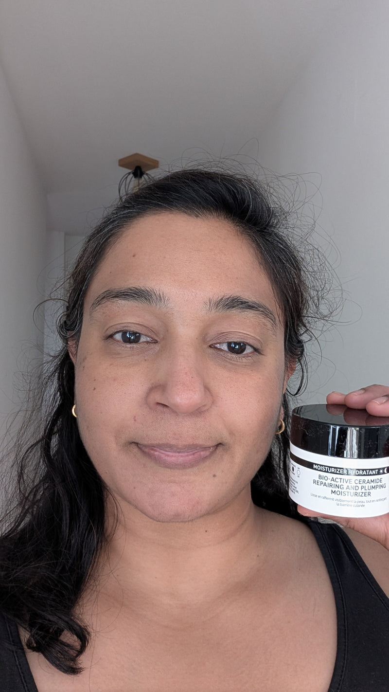 A woman holding a jar of 'The Inkey List' Bio Active Moisturiser in a home setting with a white wall and ceiling visible.