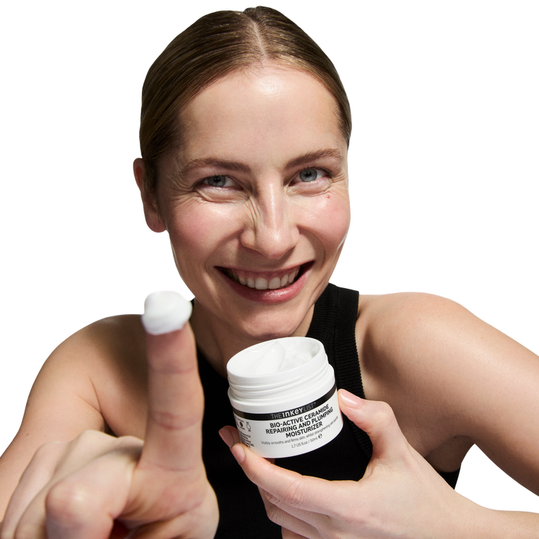Woman holding a jar of cream and a white object, with a plain background