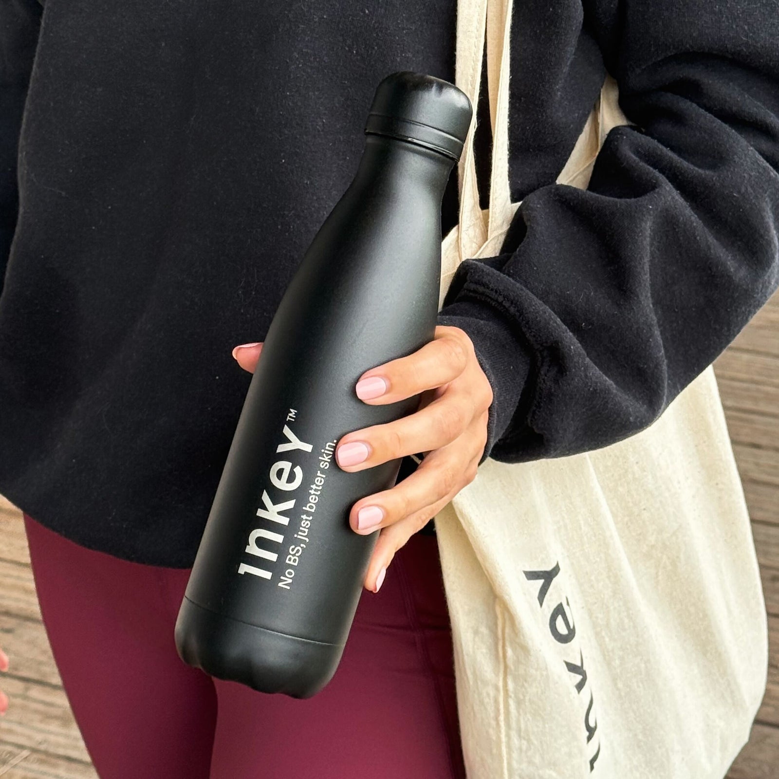 Person holding a black Inkey water bottle with a branded tote bag in the background.