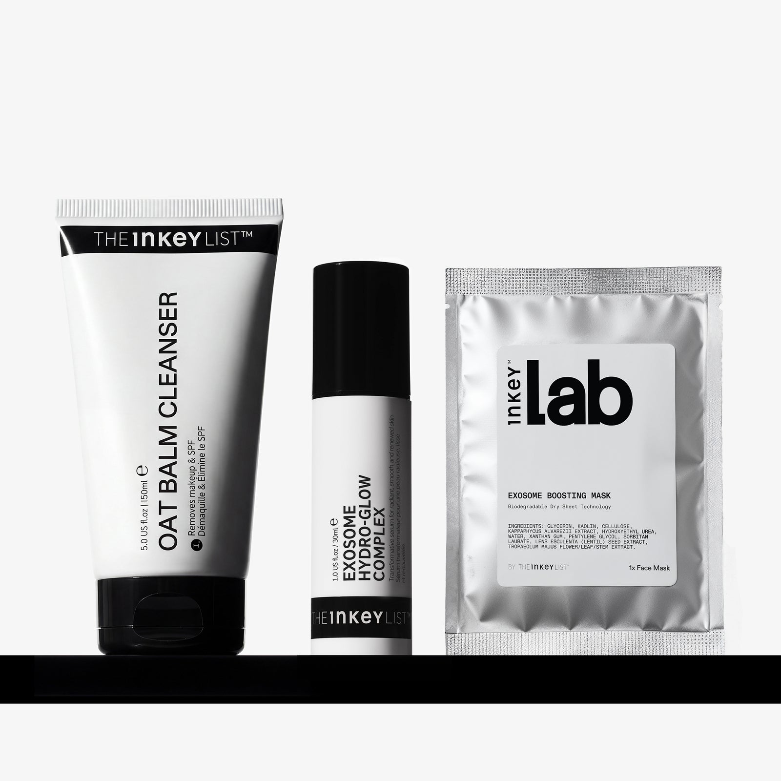 Three skincare products from The Inkey List arranged on a black shelf against a light gray background: a oat Balm Cleanser tube, an Exosome Complex Flow cream bottle, and an Exosome Boosting Mask sachet.