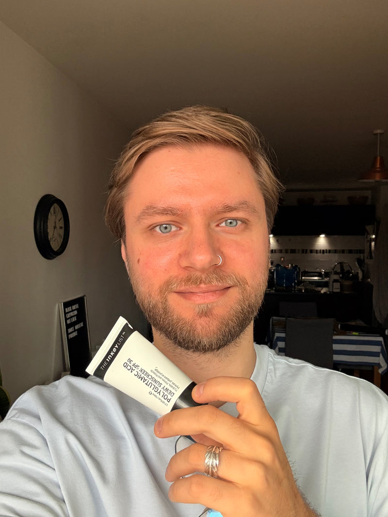 A man holding a white and black tube of 'INKEY SPF' in a home setting.