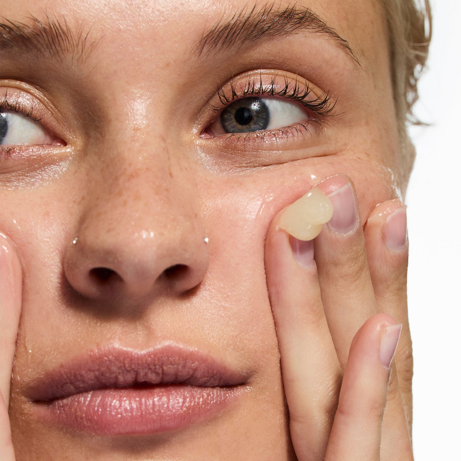 Close-up of a woman applying cream to her face with a neutral background