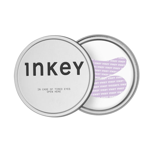 A round silver metal tin for Inkey Reusable Eye Patches on a white background, one showing the front lid with black text and the other showing the inner lid with purple text.