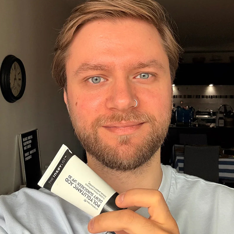 A man holding a white and black tube of INKEY SPF in a mirror selfie style.
