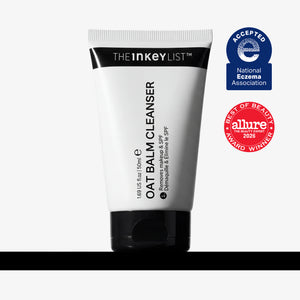 A white squeeze tube of The Inkey List Oat Balm Cleanser with a black cap, shown on a light gray background with a black bar at the bottom. Two award badges are displayed on the right: a blue National Eczema Association 'Accepted' badge and a red Allure 'Best of Beauty' award badge.