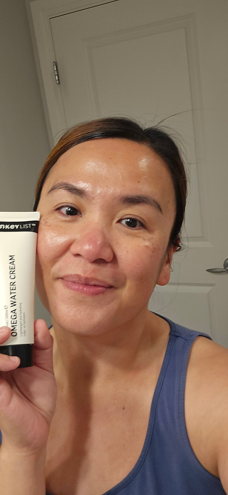 A woman holding a bottle of Omega Water Cream to her face 
