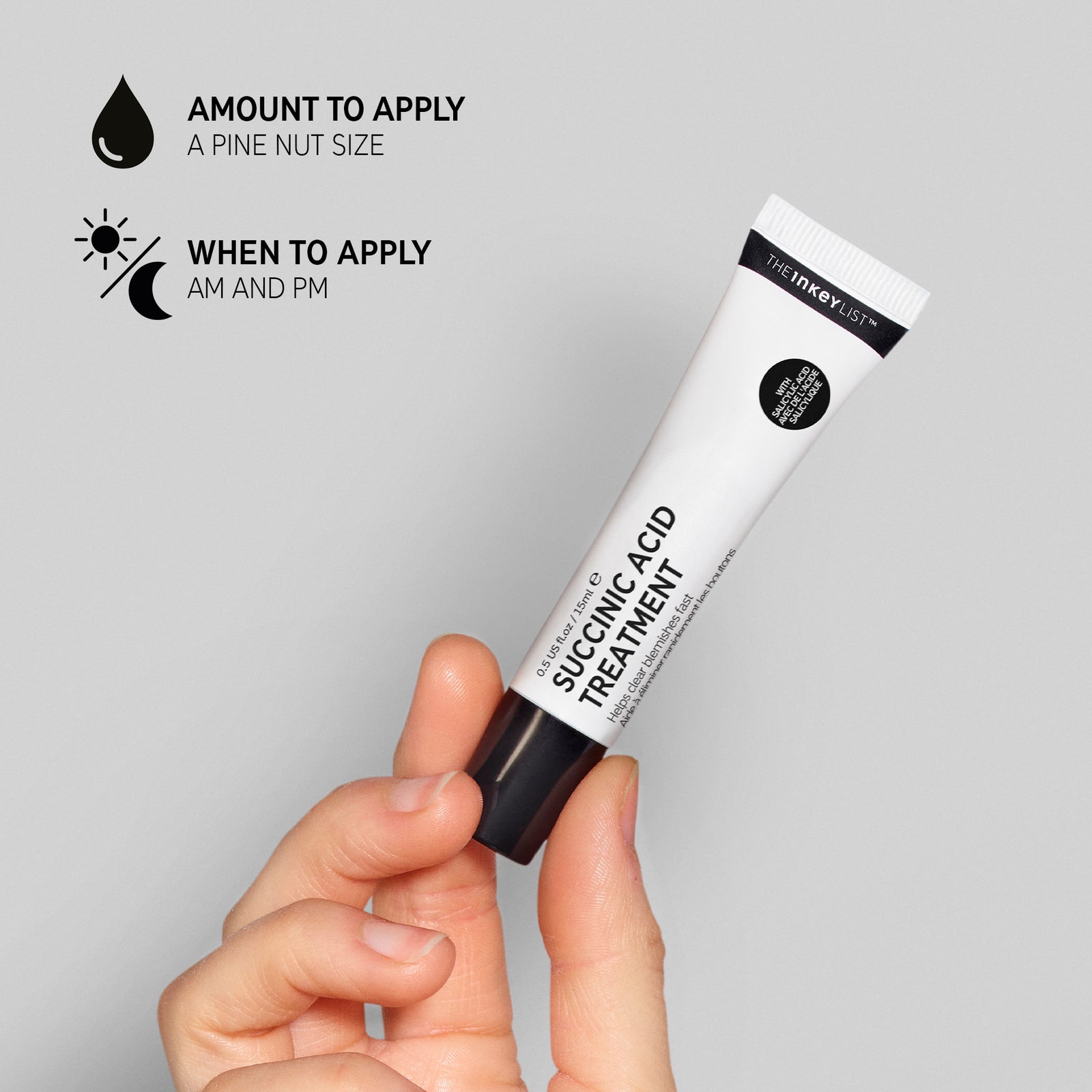 Hand holding a tube of Succinic Acid Treatment against a grey background, annotated with black text explaining amount to apply (pine nut sized) and when to apply (AM and PM) 